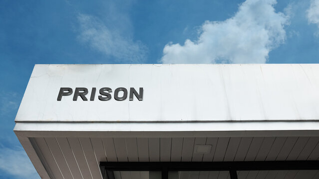 Prison word signage on a correctional facility building under a blue sky, symbolizing incarceration, law enforcement, justice system, and public security