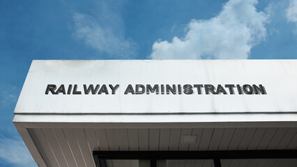 Obraz premium Railway Administration word signage on a government or transport building under a blue sky, symbolizing rail management, policy, infrastructure control, and official authority