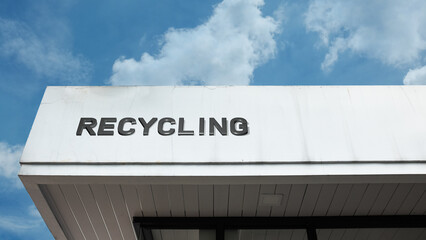 Recycling word signage on a center or industrial building under a blue sky, symbolizing environmental effort, conservation, waste management, sustainability, and resource reuse