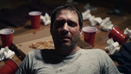 A man with a hangover waking up on the dirty floor after a party. A messy room with red plastic cups illustrates alcohol abuse.