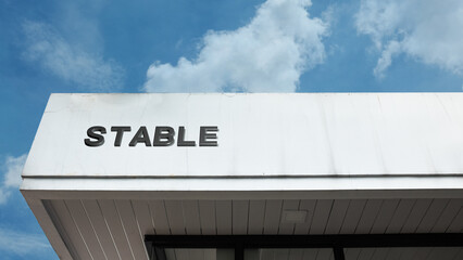Stable word signage on an agricultural or equestrian building under a blue sky, symbolizing horse housing, equestrian sport, farm life, animal care, riding facility, and rural livestock