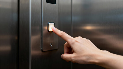 Hand pressing elevator button on metallic panel in modern building