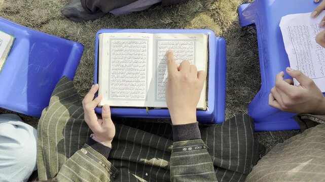 Closeup shot of a muslim boy reading holy Quran in the month of Ramadan. A little muslim student reciting holy book Quran and islamic holy book. Muslim boys reading holy Quran during pray and fast.