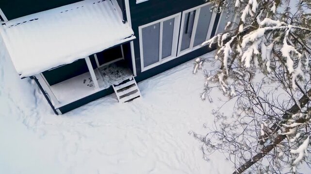 Snowy exterior view of a modern two-story house with white-framed windows and a dark facade.