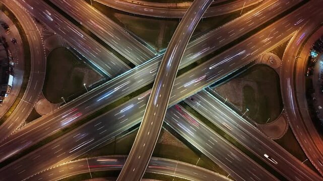 Aerial pass drifting above a wide multilane highway interchange with looping ramps and continuous vehicle light trails
