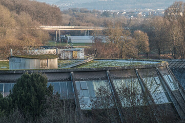 Aufsicht futuristisches Geb&auml;ude Rundsporthalle in Form eines Zylinders mit Wellblechh&uuml;tte, Fu&szlig;g&auml;ngersteg und gro&szlig;en Sprossenfenstern vor Landschaft mit Betonbr&uuml;cke in Neckartenzlingen.