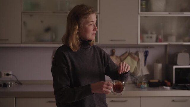 Woman with cerebral palsy stirring tea in double-walled glass mug in kitchen, demonstrating independent daily routine, calm self-care and focused, empowering domestic life. Shooting in slow motion.