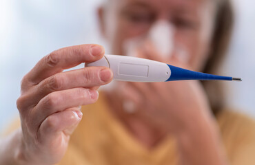 Sick person checks temperature with thermometer while experiencing cold symptoms at home in the afternoon