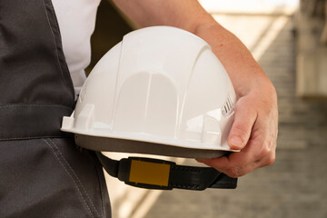 Worker holds white safety helmet in construction area during daytime, ready for task on site