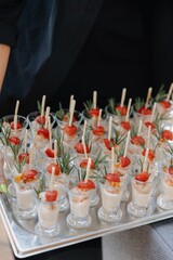 A waiter's hand holds a silver tray displaying perfect rows of small glasses containing shrimp cocktail, topped with strawberry and rosemary garnish