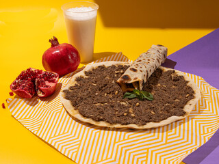 Lahmacun, Turkish Thin flatbread topped with a spicy ground meat mixture and baked in oven on bright yellow and purple background. Colorful food photography, bright color food image.