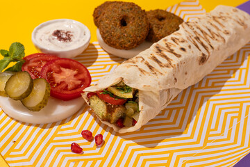 Traditional Mediterranean Arabic grilled falafel shawarma, hummus and vegetables in flatbread wraps with herbs and a variety of sauces on bright yellow color background