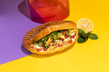Tasty chicken shawarma with vegetables, lemon and sauce in a pita bread on bright yellow and purple background. Colorful food photography, bright color food image.