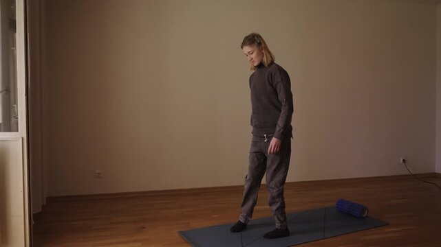 Portrait of determined young woman with cerebral palsy practicing balance and coordination exercises on yoga mat at home as part of physical therapy and rehabilitation routine, focused on recovery.