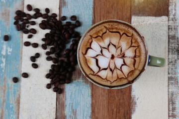 The beautiful pattern of a hot latte, along with coffee beans on multicolor vintage wooden 