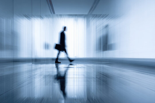 Businessman walking through modern glass office corridor motion blur effect professional corporate environment reflective floor blue tone dynamic urban confident morning