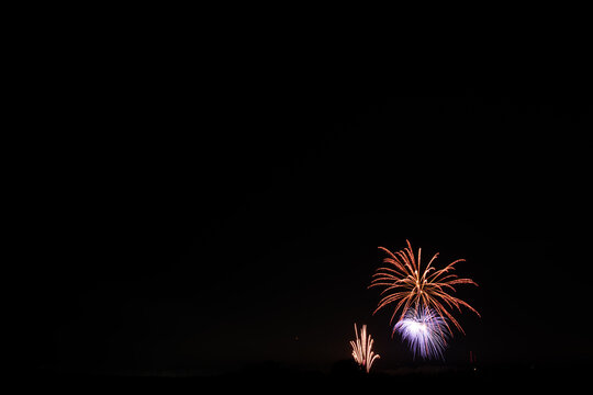 A wide photograph of purple and orange fireworks with drifting smoke, with a dark sky giving plenty of copy space.