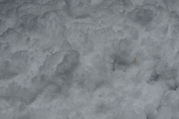 Detailed close-up view of uneven, rough snow surface showing small mounds, shadows, and natural variations in winter texture and form.