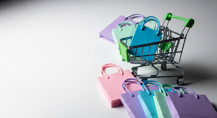 Small shopping cart with colorful paper bags. Concept: online shopping, retail, offers. Representative of e-commerce and seasonal promotions