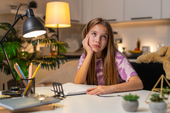 Teenager girl at night home writes diary about dreams and plans smiles thinks about goals. Caucasian child kid sitting at table at evening opens book holds pen nods makes plan for next day calmly