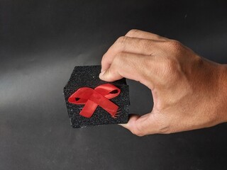 Hand holding a gift box wrapped with red ribbon on a dark background. Black Friday