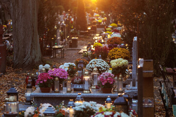 Kwiaty zdobiące nagrobki stanowią symbol pamięci, miłości i szacunku dla zmarłych. Jesienna kolorystyka w połączeniu z naturalnym światłem nadaje fotografii spokojny i nostalgiczny charakter.