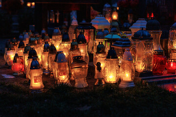 Fototapeta premium Nastrojowe ujęcie cmentarza po zmroku, gdzie jedynym źródłem światła są palące się znicze. Migoczące płomienie tworzą ciepłą, melancholijną atmosferę, podkreślając duchowy i refleksyjny wymiar miejsca