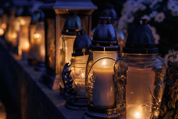 Nastrojowe ujęcie cmentarza po zmroku, gdzie jedynym źródłem światła są palące się znicze. Migoczące płomienie tworzą ciepłą, melancholijną atmosferę, podkreślając duchowy i refleksyjny wymiar miejsca