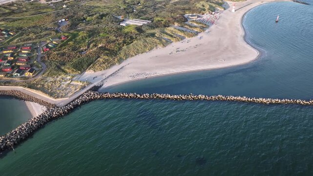 Aerial pull-back shot of D&uuml;ne, sandy sister island of Helgoland, Germany  with colorful beach houses nestle among dunes and greenery, while a long stone breakwater, sandy beach and lighthouse.