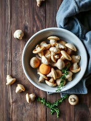 Fototapeta premium A close-up shot of a rustic wooden table with a textured grain, featuring a light grey, shallow bowl filled with an assortment of fresh shiitake mushrooms. A few loose mushrooms and sprigs of fresh or