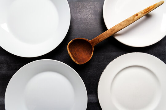 Big white plates and wooden spoon on black chalkboard background. Flat lay. Top view. Food concept. Dark mood food photography. - Powered by Adobe