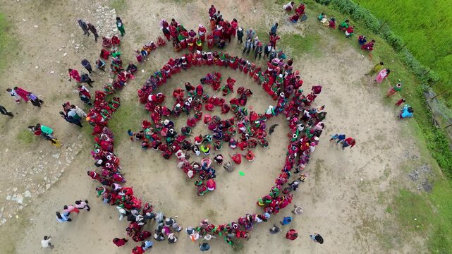 Aerial top down view of large group of Nepalese women in red sarees dancing in a circle during  festival in rural village, traditional cultural celebration and community gathering
