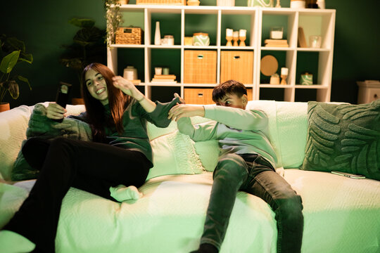 Siblings play fighting while taking smartphone selfie on couch