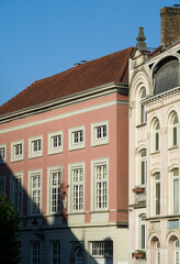 Obraz premium A pink facade in Bruges bathed in bright sunlight, creating a crisp light and shadow division. The contrast emphasizes the ornate white windows beneath the clear blue sky