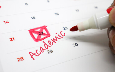 Hand Marking Academic Deadlines and Important Dates on a Calendar with a Red Marker, Symbolizing Educational Planning and Scheduling
