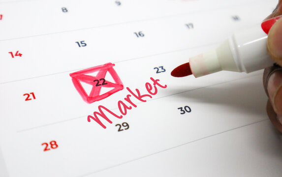 Hand marking an upcoming market event on a calendar with a red pen, highlighting important business scheduling and strategic planning for future success
