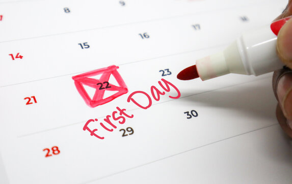 A hand uses a red marker to highlight an important date on a calendar, signifying a First Day or a new beginning and upcoming significant event