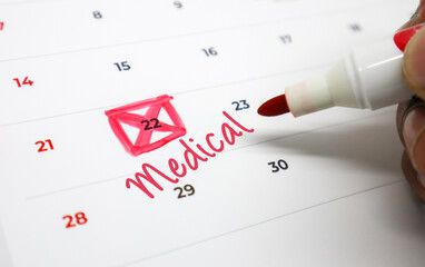 Scheduling a critical medical appointment on a desk calendar, with a hand highlighting the date in red and noting Medical for an important health reminder