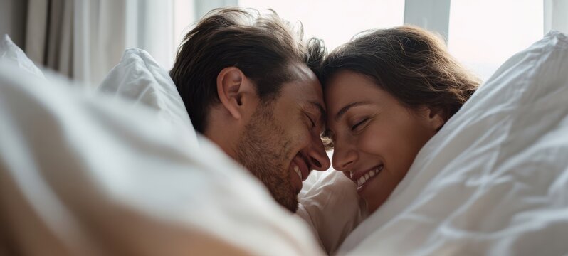 The couple sharing an intimate morning cuddle under white sheets in a sunlit bedroom