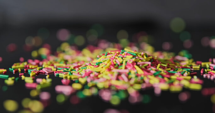 Rainbow sugar sprinkles scattering on black background, close-up, side view
