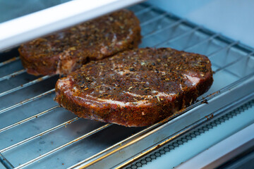 Raw ribeye steak dry brine with salt, bell pepper, and aromatic herbs rub, placed inside a fridge on a stainless steel tray
