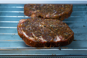 Raw ribeye steak dry brine with salt, bell pepper, and aromatic herbs rub, placed inside a fridge on a stainless steel tray