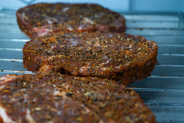 Raw ribeye steak dry brine with salt, bell pepper, and aromatic herbs rub, placed inside a fridge on a stainless steel tray