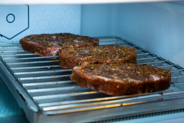 Raw ribeye steak dry brine with salt, bell pepper, and aromatic herbs rub, placed inside a fridge on a stainless steel tray