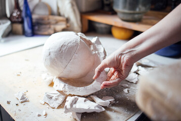 Female artist carefully removing plaster mold from a sculpted piece, surrounded by artistic tools and materials, showcasing the intricate process of sculpture creation