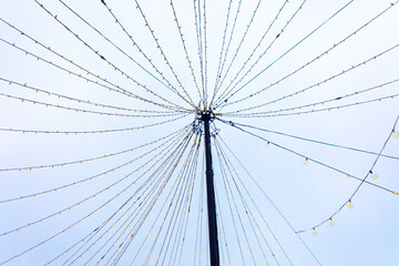 Strings of lights radiate symmetrically from a tall central pole, forming a festive canopy against pale sky. Geometric pattern creates a striking starburst effect with balanced visual rhythm