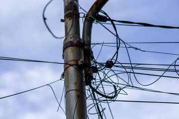 Low angle view of rusty power poles, tangled wires, and blue sky. Close up of old rusty electric post with disorganized tangled cables representing bad infrastructure.