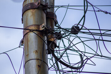 Low angle view of rusty power poles, tangled wires, and blue sky. Close up of old rusty electric post with disorganized tangled cables representing bad infrastructure.