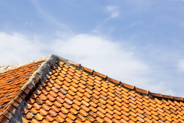 Orange clay roof tiles on blue sky background. Traditional terracotta roof pattern on residential roof.