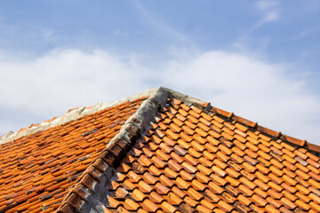 Orange clay roof tiles on blue sky background. Traditional terracotta roof pattern on residential roof.